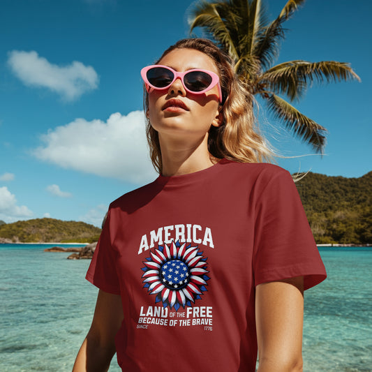Person wearing a red t-shirt with 'America' text and design, sunglasses, standing on a beach with palm trees and clear water.